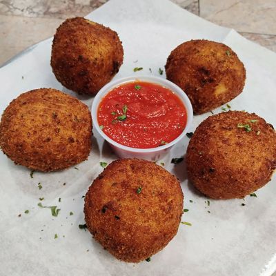 Four fried rice balls with a cup of marinara sauce