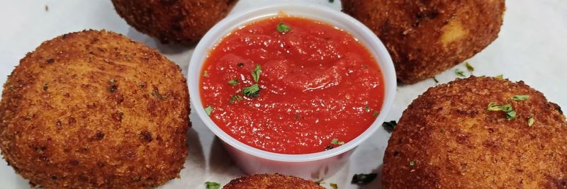 Four fried rice balls with a cup of marinara sauce